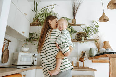 Mother carrying son in kitchen at home - WESTF25352