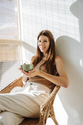 Porträt einer glücklichen Frau mit Kaffeetasse, die sich im Stuhl entspannt - WESTF25363