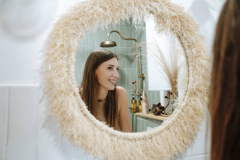 Smiling woman looking at herself in bathroom mirror - WESTF25364