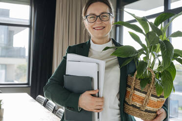 Lächelnde Geschäftsfrau mit Topfpflanze und Aktenordner im Büro - OSF02352