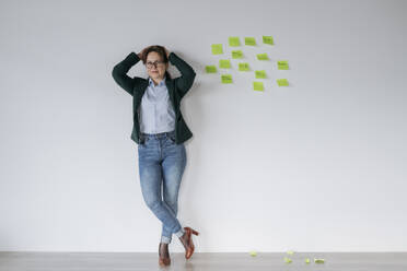 Businesswoman leaning on white wall near notes in office - OSF02355