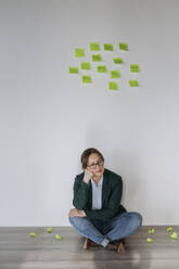 Thoughtful businesswoman sitting on ground in office - OSF02357