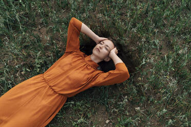 Thoughtful woman with hand in hair lying in field - TOF00170