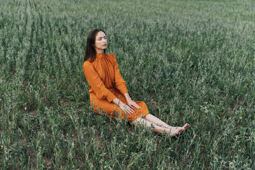 Thoughtful woman sitting amidst crops in corn field - TOF00173