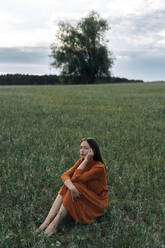 Nachdenkliche Frau sitzt in einem grünen Maisfeld - TOF00174