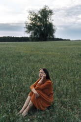 Thoughtful woman sitting in green corn field - TOF00174