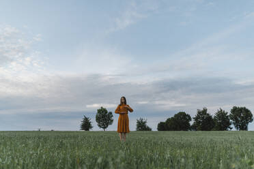 Frau inmitten von Maiskörnern auf einem Feld vor dem Himmel bei Sonnenuntergang - TOF00185