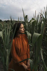 Nachdenkliche Frau inmitten von Maispflanzen auf einem Feld - TOF00225
