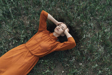 Thoughtful woman with head in hands lying in field - TOF00248