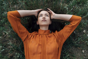 Thoughtful woman with head in hands lying in field - TOF00249