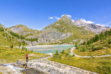 Mature woman hiking near Margaritze reservoir under sky at Hohe Tauern national park, Salzburg, Austria - FOF13732