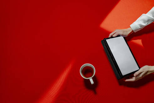 Hände einer Frau mit Tablet-PC und Teetasse über einem roten Tisch - MBLF00224