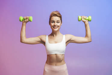 Happy woman with dumbbells exercising against colored background - OIPF03655