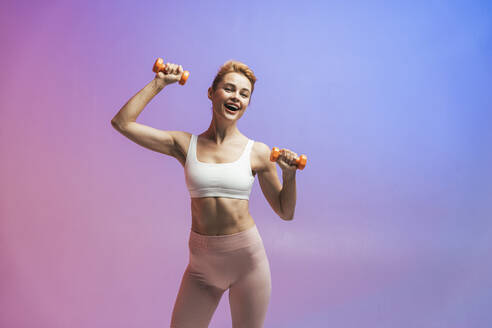 Happy woman exercising with dumbbells against two tone colored background - OIPF03663