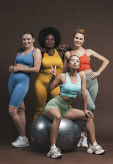 Smiling multiracial female friends with fitness ball against brown background - OIPF03766