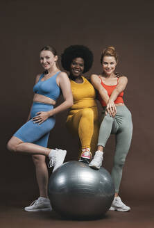 Lächelnde multirassische Freunde mit Fitnessball vor braunem Hintergrund - OIPF03768