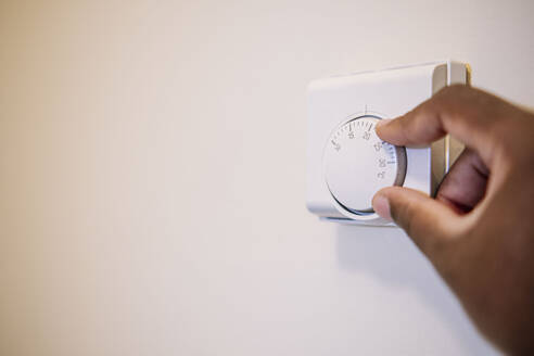 Hand eines Mannes, der die Temperatur des Thermostats zu Hause einstellt - AMWF01959