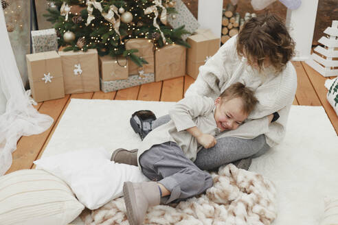 Mutter kitzelt glücklichen Sohn auf Teppich zu Hause - EHAF00166