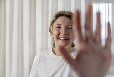 Happy woman showing stop gesture in front of white curtain - MBLF00229