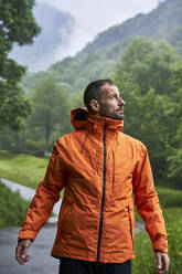 Nachdenklicher Mann mit orangefarbener Jacke und vor einem Berg stehend - VEGF06229