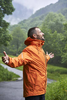 Glücklicher Mann in orangefarbener Jacke vor einem Berg in den Pyrenäen - VEGF06231