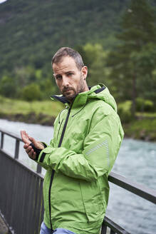 Mann mit grüner Jacke, der sich an ein Geländer in der Nähe des Flusses lehnt - VEGF06245
