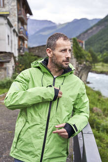 Mann mit grüner Jacke und stehend an einem Geländer vor einem Gebirge - VEGF06247