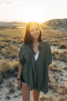 Lächelnde junge Frau, die bei Sonnenuntergang durch eine Wüstenlandschaft läuft - DAMF01248