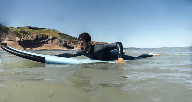 Mann mit Surfbrett auf dem Meer unter klarem blauen Himmel - DAMF01263