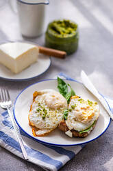 High angle of plate of healthy toast with fried egg pesto sauce green herbs and cheese served on gray table during breakfast - ADSF51798