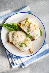 Top view of plate of appetizing toast with fresh spinach leaves fried eggs pesto sauce served on blue napkin - ADSF51799