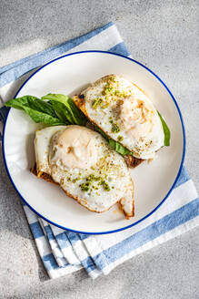 Draufsicht auf einen Teller mit appetitlichem Toast mit frischem Blattspinat, Spiegeleiern und Pestosauce, serviert auf einer blauen Serviette - ADSF51799