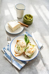 High angle of plate of healthy toast with fried egg pesto sauce green herbs and cheese served on gray table during breakfast - ADSF51801