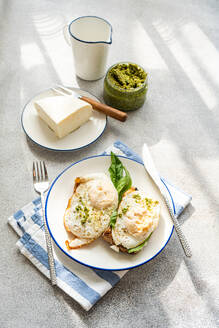 Hohe Winkel der Platte von gesunden Toast mit Spiegelei Pesto-Sauce grünen Kräutern und Käse serviert auf grauen Tisch beim Frühstück - ADSF51801