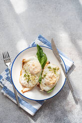 Top view of plate of healthy toast with fried egg pesto sauce and green herbs served on gray table during breakfast - ADSF51802