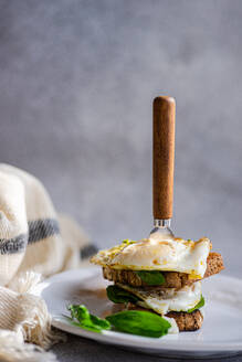 Teller mit gesundem Toast mit Spiegelei-Pesto-Sauce grünen Kräutern auf grauem Tisch beim Frühstück - ADSF51803