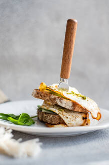 Plate of healthy toast with fried egg pesto sauce green herbs on gray table during breakfast - ADSF51805