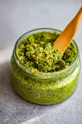 Von oben frischer grüner Pesto-Sauce und Holzlöffel auf dem Tisch bei der Vorbereitung einer gesunden Mahlzeit zu Hause - ADSF51806