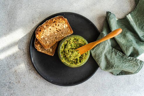 Draufsicht auf hausgemachtes leckeres Brot und Pesto-Sauce mit Holzlöffel auf grauem Tisch in der Nähe von Serviette platziert - ADSF51808