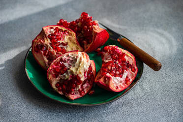 From above fresh pomegranate pieces with vibrant red seeds on a green ceramic plate set against a textured grey concrete background - ADSF51810