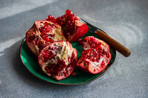 From above fresh pomegranate pieces with vibrant red seeds on a green ceramic plate set against a textured grey concrete background - ADSF51810