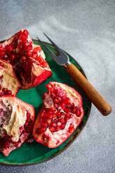 From above fresh pomegranate pieces with vibrant red seeds on a green ceramic plate set against a textured grey concrete background - ADSF51811