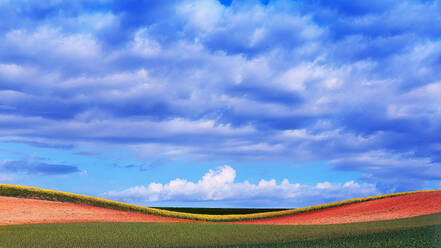 Vielschichtige Landschaft mit hügeligen Feldern unter einem dramatischen Himmel, der ein Spektrum von Farben von der Erde bis zum Himmel zeigt - ADSF51909