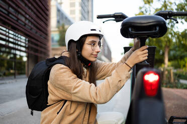 Eine konzentrierte junge Frau mit Helm schließt ihr Fahrrad in einer städtischen Umgebung ab, bereit für einen anstrengenden Tag. - ADSF52004