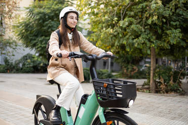 Eine junge Frau mit Helm fährt auf einem grünen Elektrofahrrad durch die Stadt und wirbt für einen umweltfreundlichen Stadtverkehr. - ADSF52005