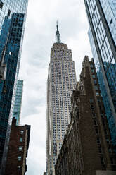 Von unten von modernen Hochhäusern mit verspiegelten Glaswänden und Empire State Building gegen bewölkten Himmel in New York City bei bedecktem Wetter am Tag - ADSF52018