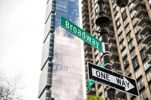 Niedriger Winkel von Broadway Lage Richtung und Einbahnstraße Schilder auf Wegweiser gegen verschwommene Hochhäuser mit Glaswänden in Manhattan, New York City im Sommer tagsüber unter blauem Himmel befestigt. - ADSF52020