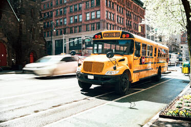 Leuchtend gelber Schulbus auf einer Kreuzung auf der belebten Straße von Manhattan in der Innenstadt von New York Stadt in der Nähe von fahrenden Auto - ADSF52031