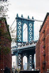 Ein malerischer Blick auf die Manhattan Bridge von einer Kopfsteinpflasterstraße in DUMBO, Brooklyn, aus gesehen, mit historischen Gebäuden auf beiden Seiten. - ADSF52041