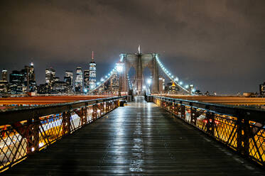 Night view of the Brooklyn Bridge walkway leading to the sparkling Manhattan skyline. - ADSF52042